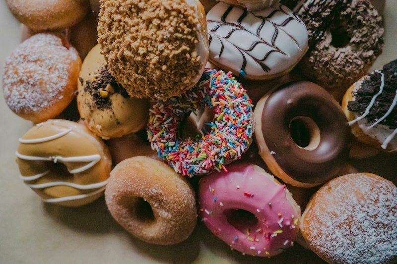 Assortment of freshly baked artisanal glazed donuts with chocolate toppings, sprinkles, and caramel.
