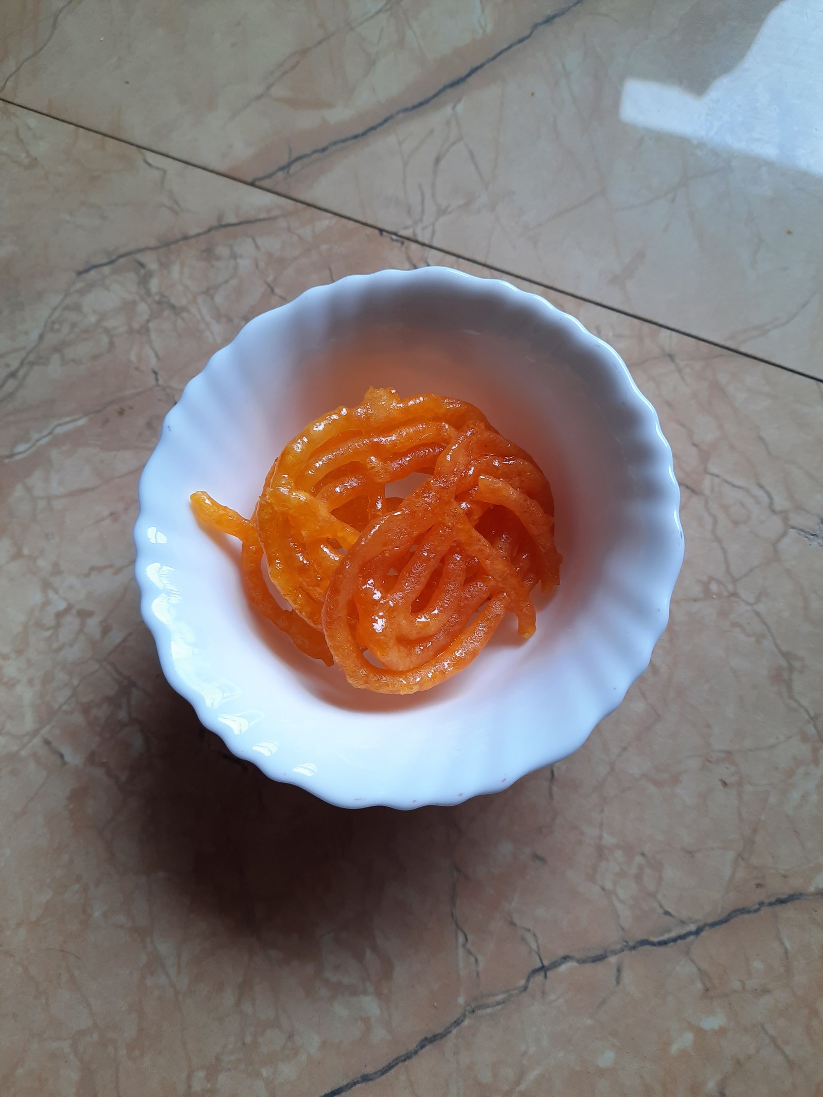 Crisp spiral golden Pure Ghee Jalebi soaked in saffron cardamom syrup served in a traditional bowl.